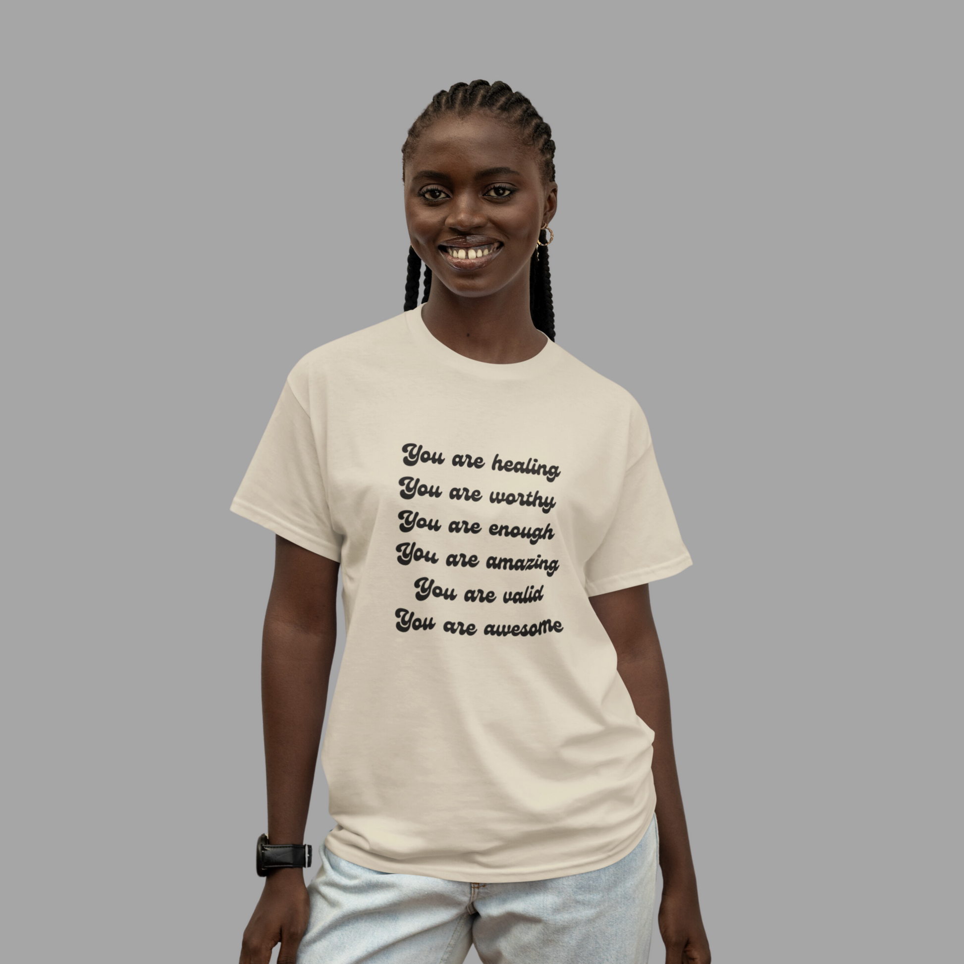 A smiling woman wearing a You are Healing Unisex Heavy Cotton T-shirt with an empowerment message that reads: "you are healing, you are worthy, you are enough, you are amazing, you are valid, you are awesome.