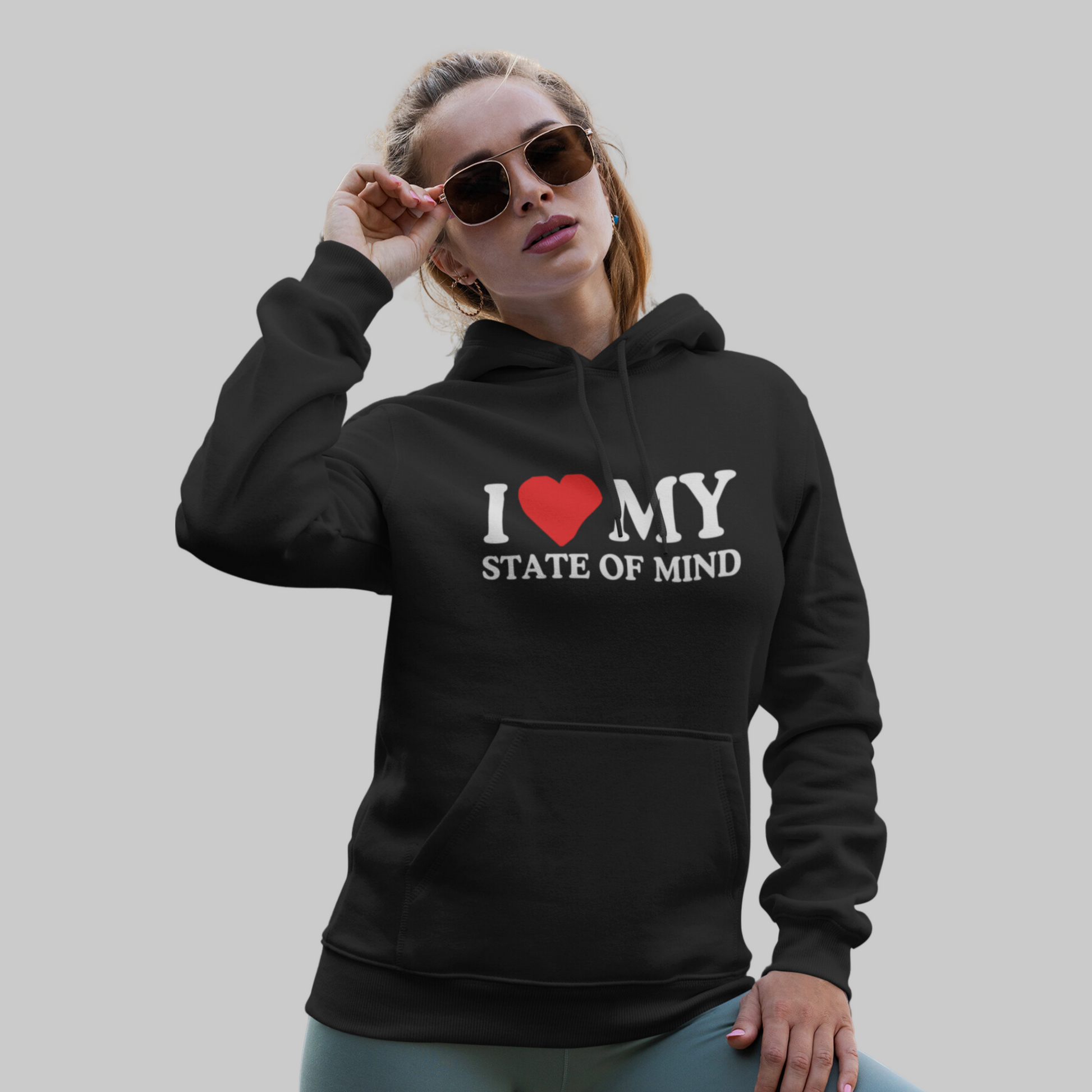 Woman in a stylish black State of Mind Unisex Heavy Blend Hooded Sweatshirt emblazoned with empowering quotes including "i ❤️ my state of mind," confidently adjusting her sunglasses, exuding confidence and support.