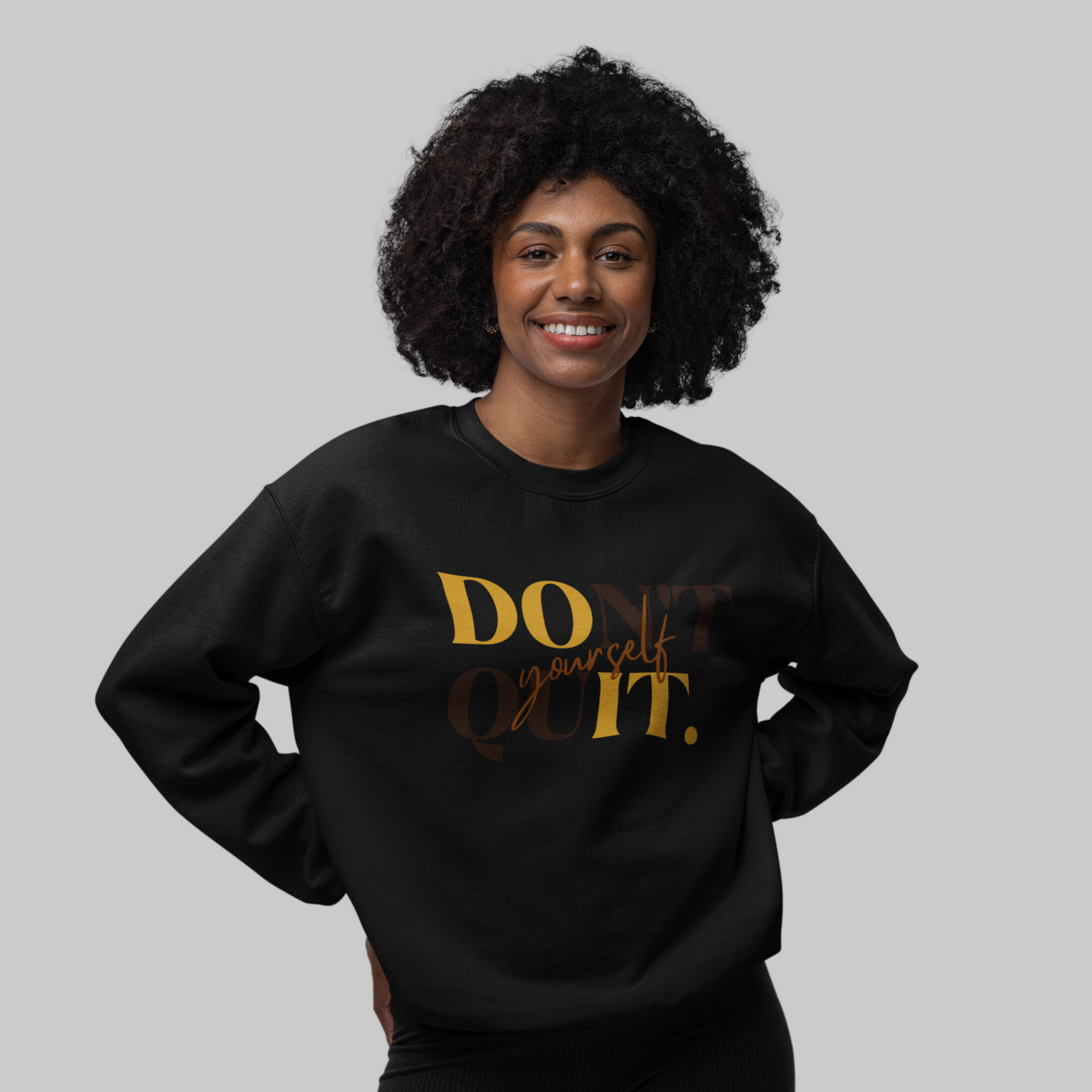 A smiling woman with curly hair wearing a black DOn't quIT Yourself Unisex Crewneck Sweatshirt featuring the supportive quote "don't quit your daydream" in gold letters for mental health awareness.