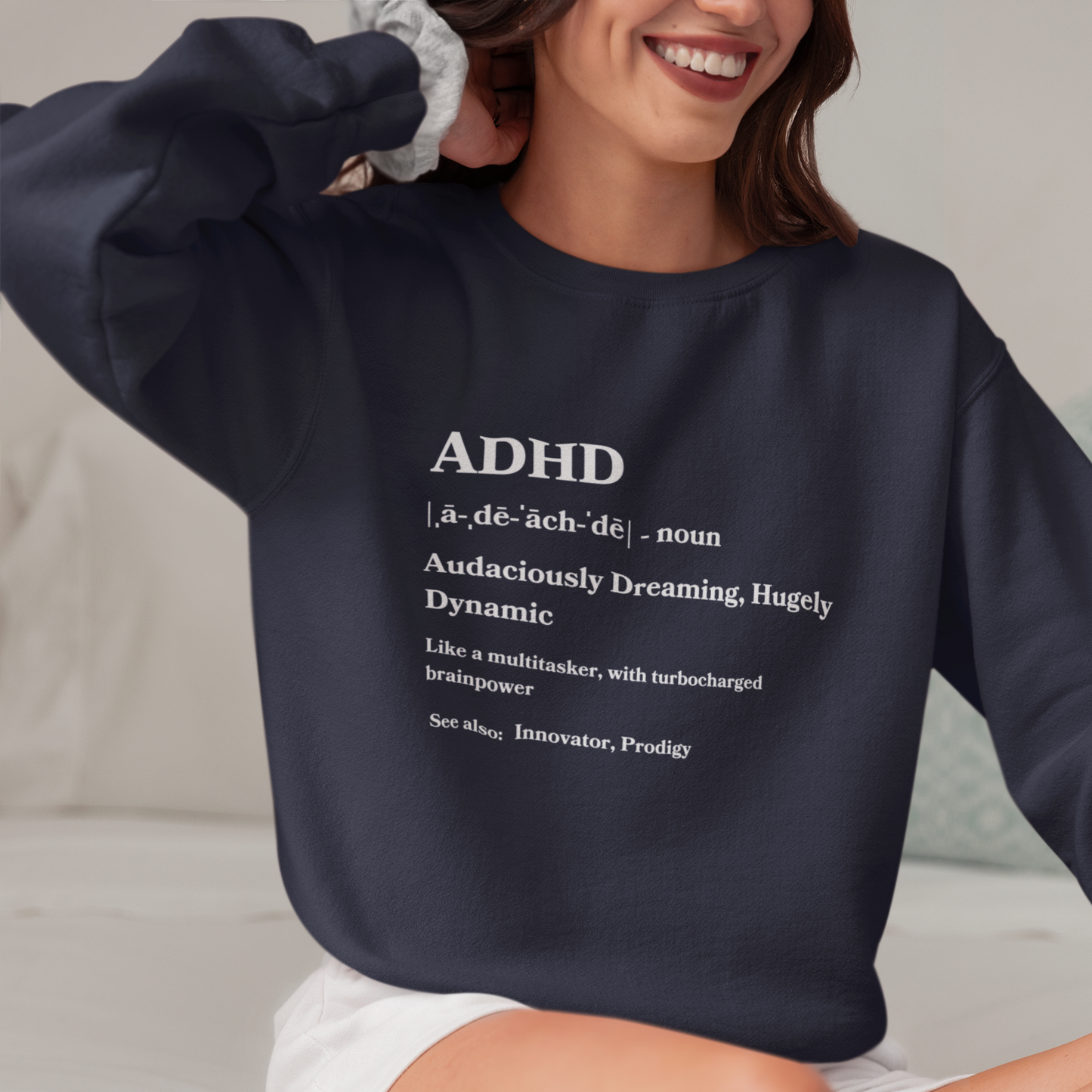 A smiling woman wearing a navy blue ADHD Definition Unisex Sweatshirt with "adhd" defined in white text as "audaciously dreaming, hugely dynamic" and other descriptive terms.