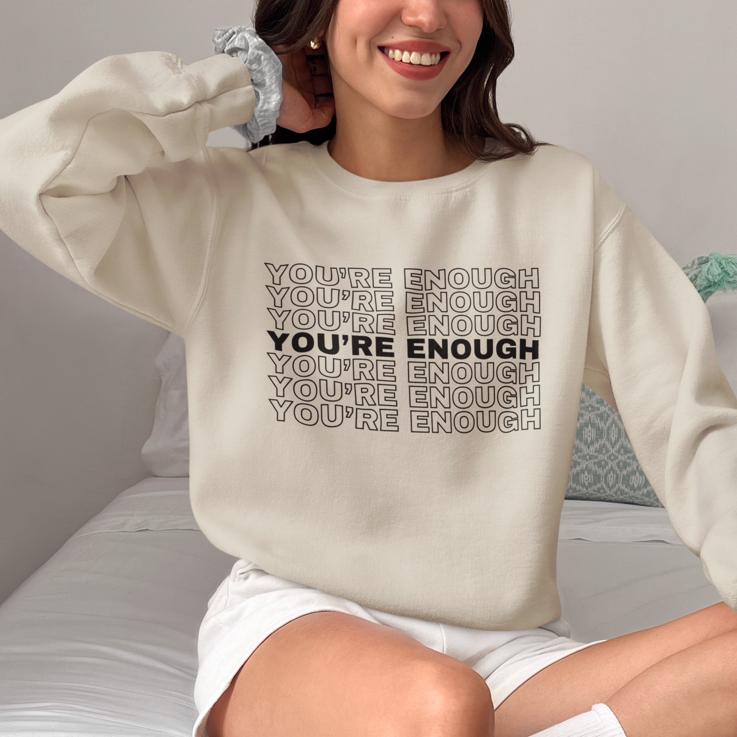 A woman sitting on a bed, embodying empowerment in the You're Enough Unisex Heavy Blend Crewneck Sweatshirt.